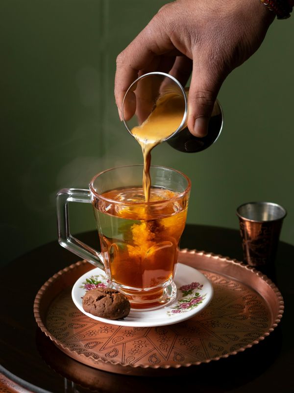 Desi chai being poured into a floral glass cup on an engraved copper tray — Pakistani tea recipe