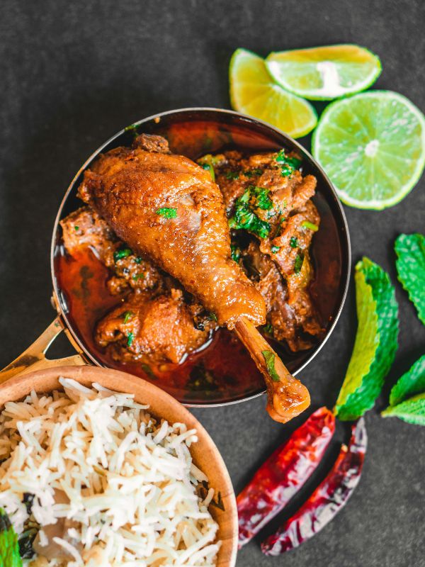 Bone-in chicken karahi in a steel pan with white rice, red chillies and lime — Pakistani main dish recipe